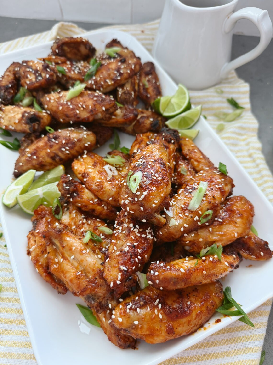 sweet and spicy korean wings with sesame seeds and limes on white tray