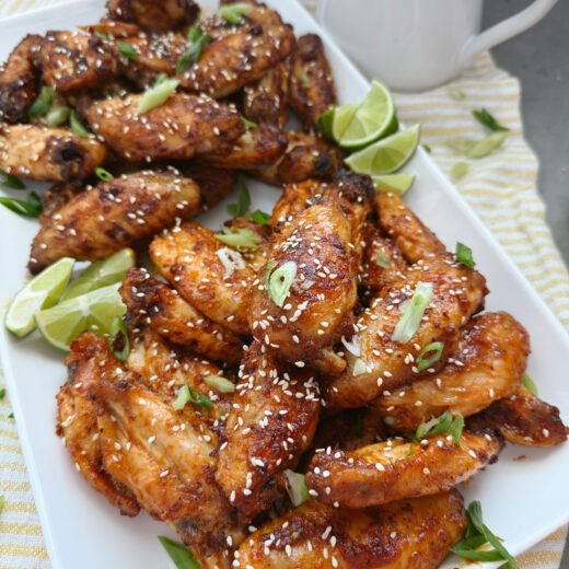 sweet and spicy korean wings with sesame seeds and limes on white tray