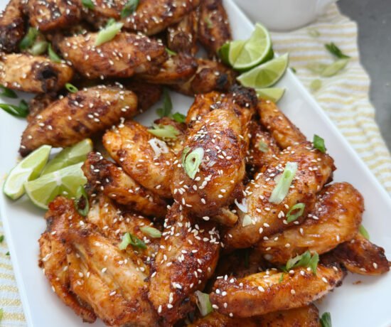 sweet and spicy korean wings with sesame seeds and limes on white tray